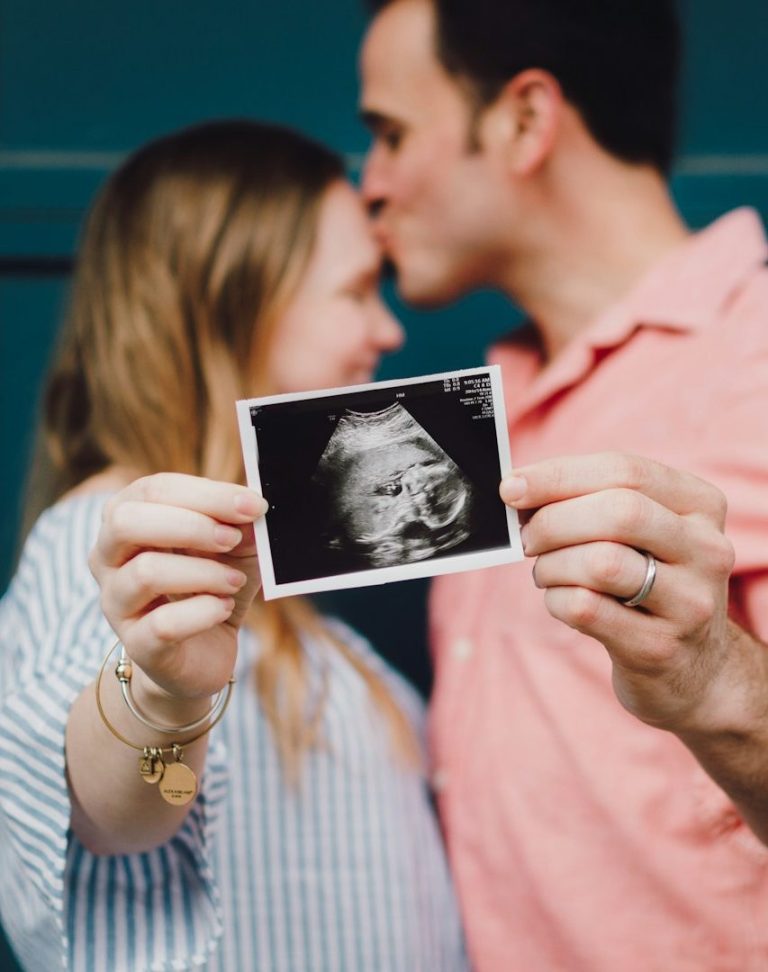 Paar hält Ultraschallbild eines Babys vor sich und küsst sich.