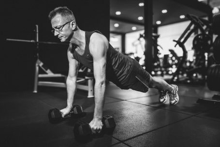Mann macht Liegestütze mit Hanteln in einem modernen Fitnessstudio.
