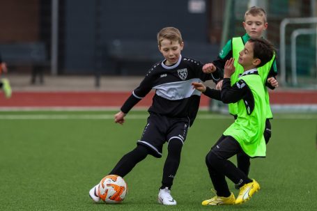 Zwei Kinder beim Fußballspielen, ein Kind dribbelt, das andere versucht, den Ball zu erobern.