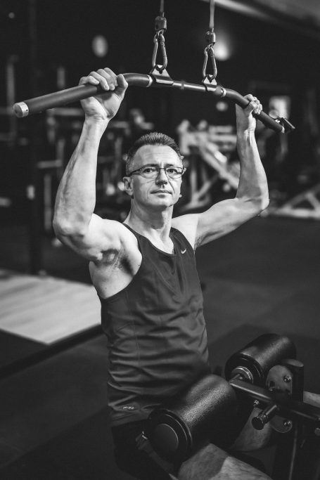 Mann trainiert im Fitnessstudio an einer Zugmaschine mit Hantelstange.