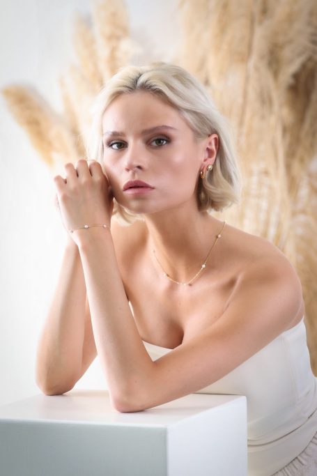 Junge Frau mit blonden Haaren, elegant in einem schlichten Kleid, wirkt nachdenklich.