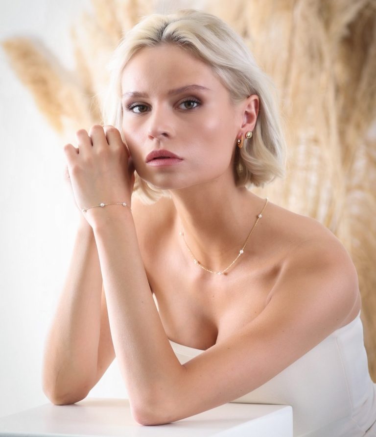 produktfotografie in krefeld businessfotograf adler photographie fotostudio Junge Frau mit blonden Haaren trägt eleganten Schmuck vor einem neutralen Hintergrund.