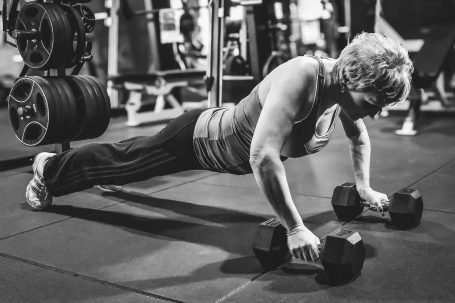 Ältere Frau macht Liegestütze mit Kurzhanteln im Fitnessstudio.
