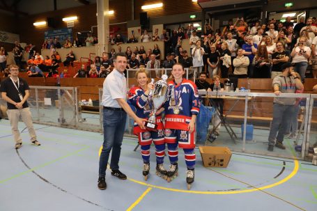 Zwei Sportler in Trikots halten einen Pokal und posieren mit einem Veranstalter.