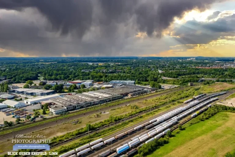Blick auf einen Güterbahnhof mit Wolken und grünem Umland.