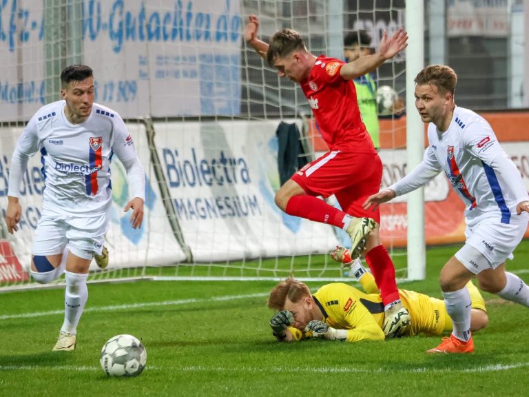 Eventfotograf Krefeld adler photographie Fußballspiel: Spieler springt über einen Torwart, andere Spieler im Hintergrund.