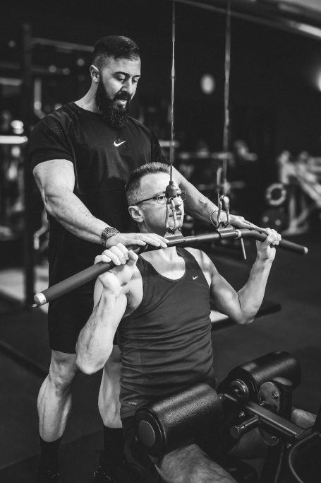 Zwei Männer im Fitnessstudio, einer hilft dem anderen beim Gewichtheben.