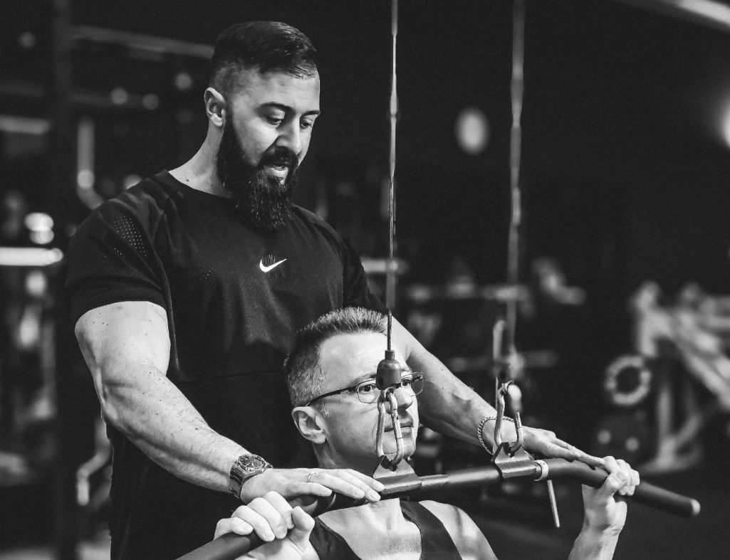 businessshooting adler photographie Ein Trainer beaufsichtigt einen Mann beim Bankdrücken im Fitnessstudio.