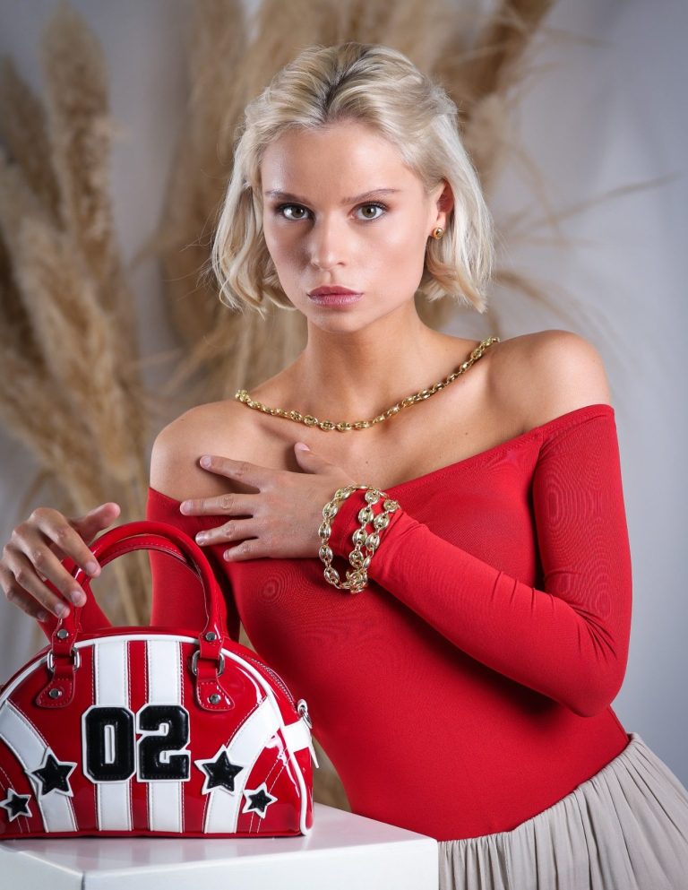 produktfotografie in krefeld businessfotograf adler photographie fotostudio Blonde Frau in rotem Oberteil mit gestreifter Tasche und Goldschmuck.