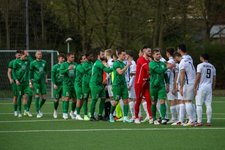 Zwei Mannschaften in grünen und weißen Trikots stehen sich auf dem Fußballfeld gegenüber.