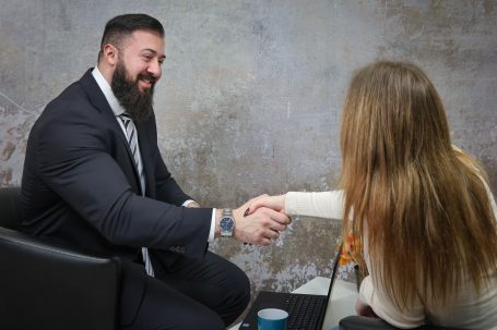 Mann im Anzug schüttelt einer Frau dankbar die Hand in einem geschäftlichen Umfeld.