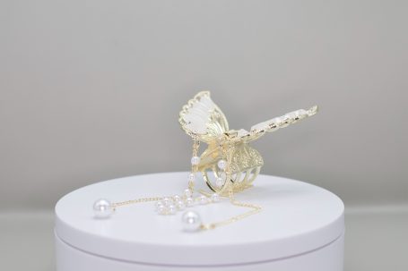 Goldene Schmetterlingsfigur mit Perlen auf einer weißen Basis.