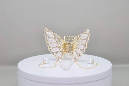 Ein filigraner Schmetterling aus goldfarbenem Draht mit weißen Elementen.