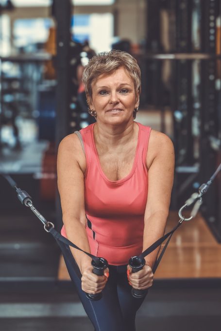 Eine lächelnde Frau in einem Fitnessstudio trainiert mit Kabelzügen.