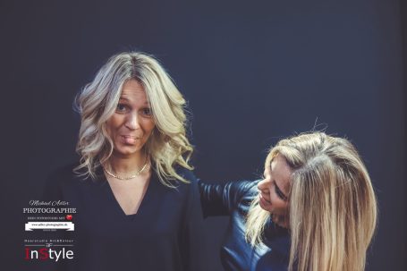 Zwei Frauen mit blonden Haaren posieren lächelnd vor einem dunklen Hintergrund.