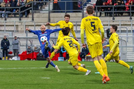 Ein Fußballer in blauer Kleidung wird von Spielern in gelber Kleidung angegriffen.