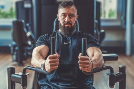Mann mit Bart trainiert an einer Fitnessmaschine, hält die Griffe fest.
