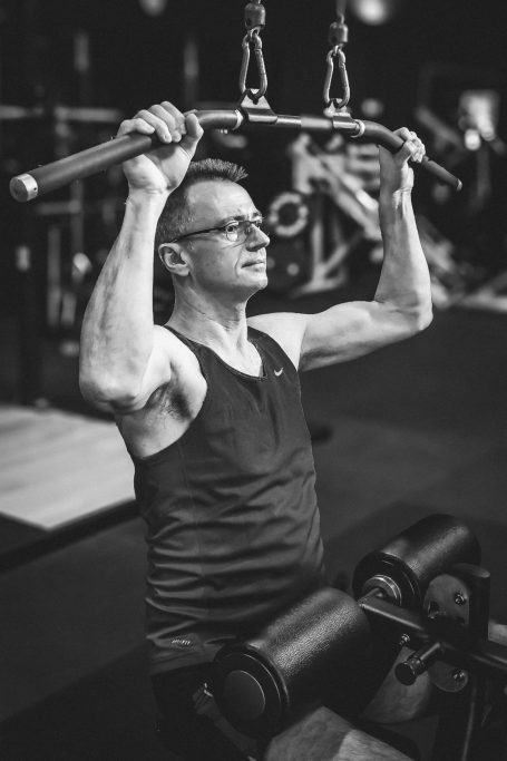 Mann führt Klimmzüge in einem Fitnessstudio aus, trägt ein schwarzes Tanktop.