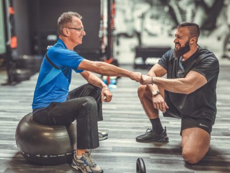 Adler Photographie krefeld Zwei Männer in einem Fitnessstudio, einer sitzt auf einem Gymnastikball, der andere kniet.