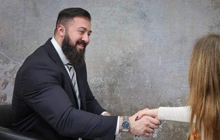 Businesshooting krefeld adler photographie Ein Mann mit Bart schüttelt einer Person die Hand, lächelnd, in einem Bürosetting.