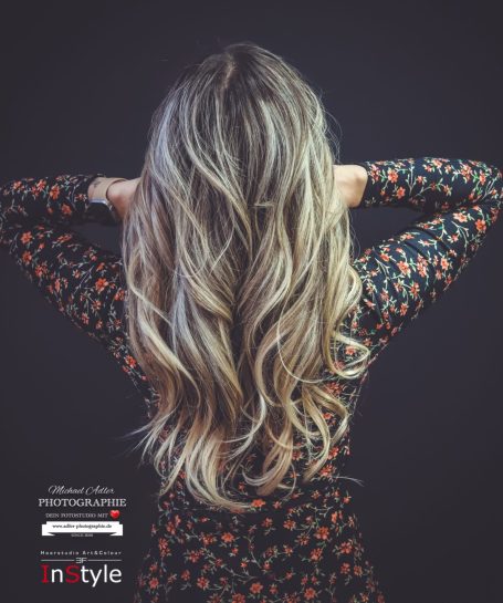 Lange, lockige Haare einer Person, die von hinten in einem Blumenkleid zu sehen ist.