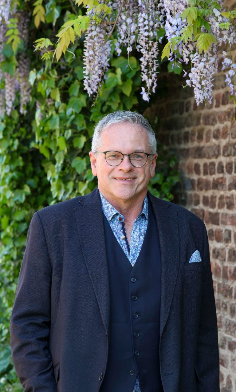 Businesshooting krefeld adler Photographie Mann mit Brille und grauem Haar in eleganter Kleidung vor einer Weinpflanze.