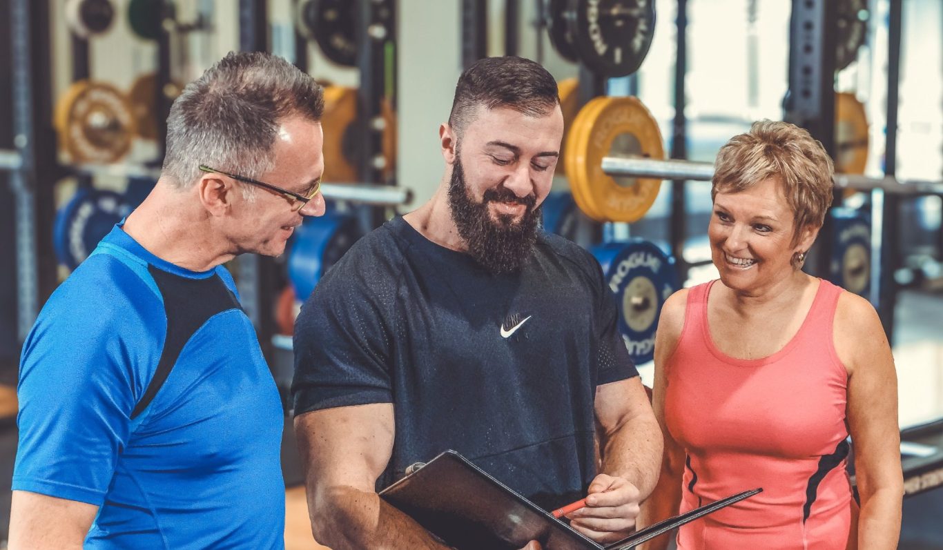 businessshooting adler photographie Drei Personen in einem Fitnessstudio, dabei eine Diskussion und Trainingsplanung.