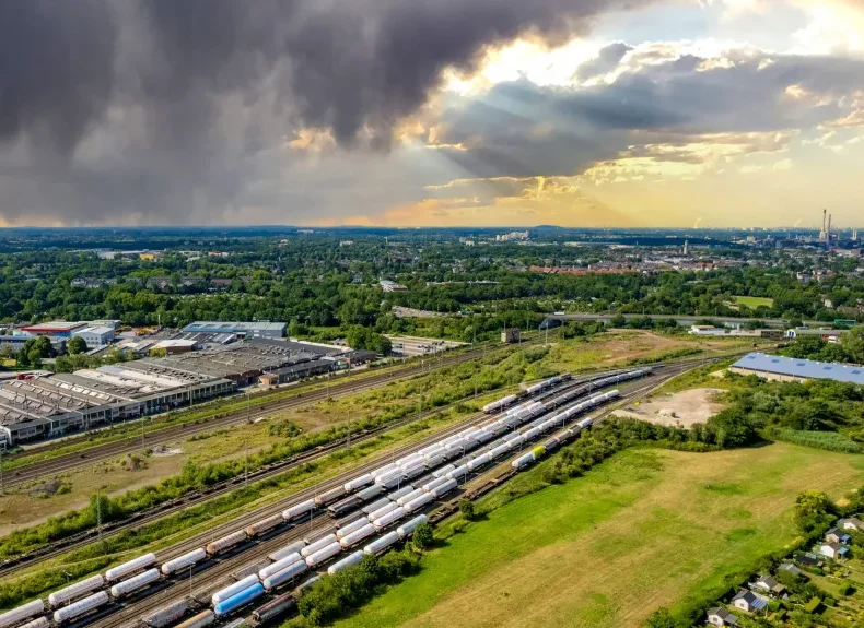 Drohnen fotografie Adler photographie Blick auf ein weitläufiges Bahn-Gelände mit Wolken am Himmel und grüner Umgebung.