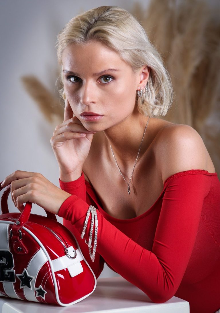produktfotografie in krefeld businessfotograf adler photographie fotostudio Eine blonde Frau in rotem Oberteil posiert mit einer roten Tasche.