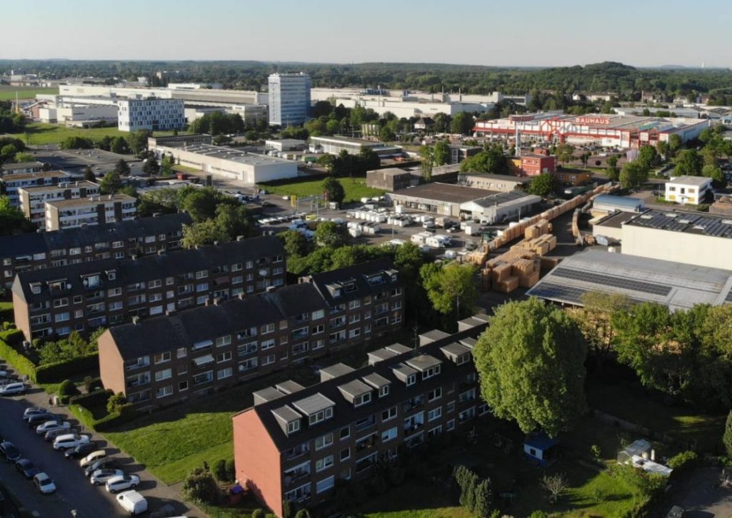Professionelle Drohnen Fotografie bei Adler Photographie Krefeld Luftaufnahme einer Stadt mit Wohngebäuden und Industrieanlagen im Hintergrund.