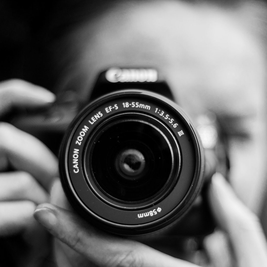 Adler Photographie Krefeld Eine Person hält eine Kamera und blickt direkt in das Kameraobjektiv.