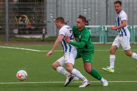 Ein Spieler in blauer und weißer Kleidung wird von einem Torwart in grüner Kleidung festgehalten.
